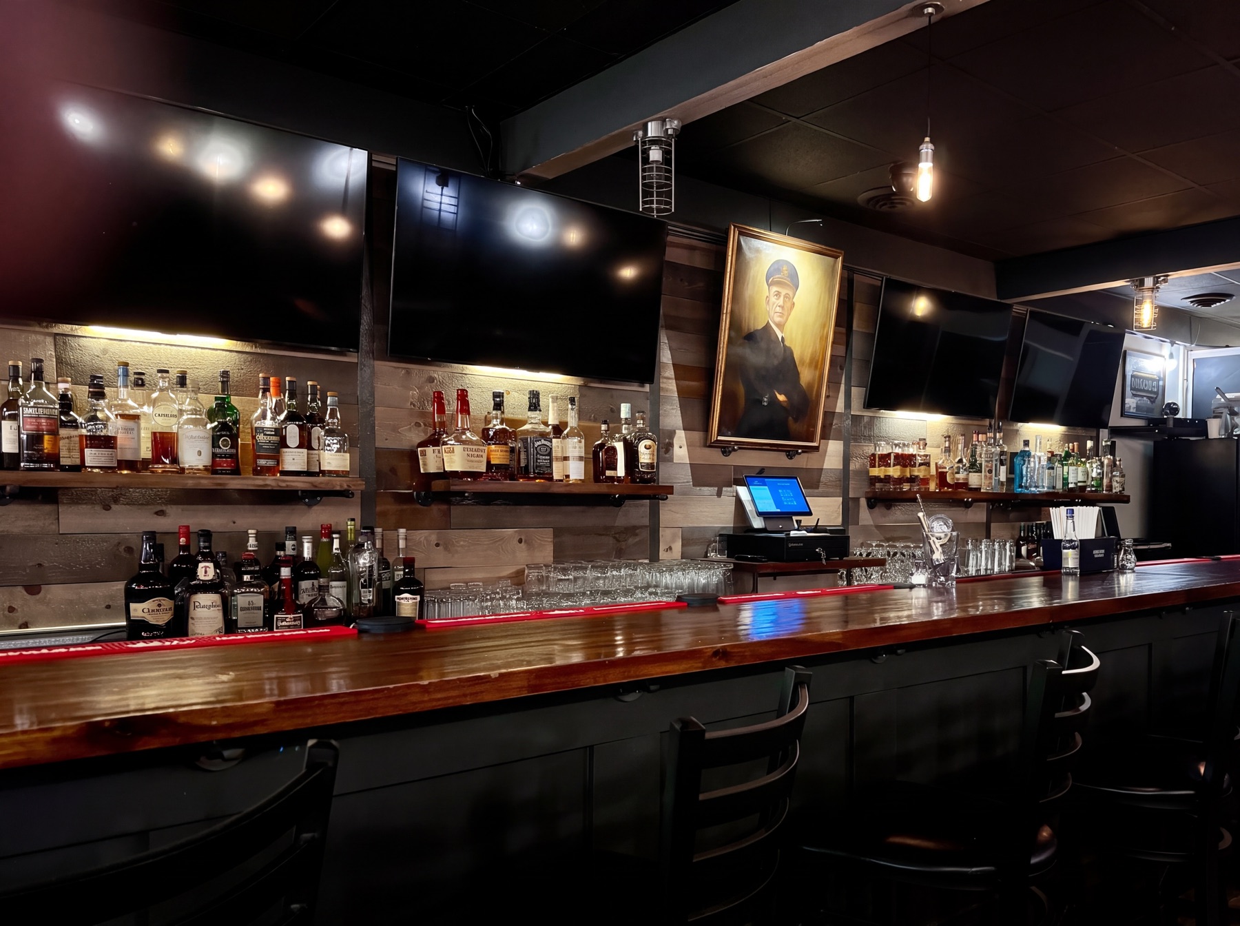The Control Car Bar: full liquor shelves, the framed Commander Weyerbacher painting above the register, and the red-lit bar counter