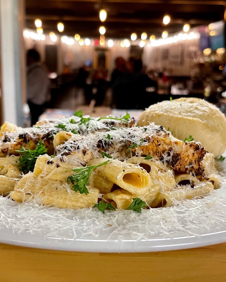 Creamy chicken pasta entree with dining room bokeh behind it